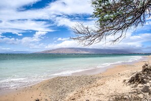A beach with clear turquoise water, a sandy shore, and a distant mountain.