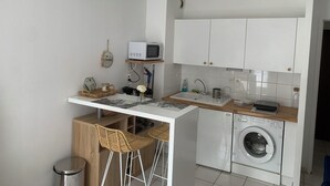Cocina compacta con microondas, pileta y lavadora. Cuenta con un pequeño sector bar con taburetes y un espejo decorativo.