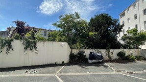 Un estacionamiento con espacios delimitados, una pared blanca con vegetación y un edificio al fondo.