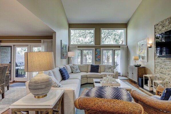 A living room with a sofa, a coffee table, a lamp, wicker chairs, and artwork on the walls.