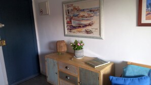 A room with a wooden cabinet, a framed painting of a boat, a potted plant, and a book on the cabinet. - Apartamento con Encanto al Lado de la Playa El Golfet (Calella de Palafrugell)