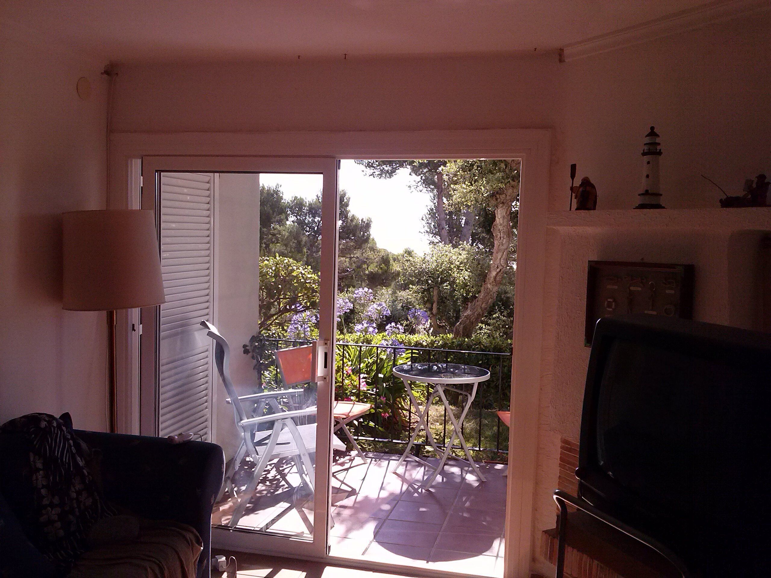 A living room with a sliding glass door leading to a patio. There is a TV on the right, a lamp on the left, and a chair near the door.