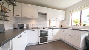 A modern kitchen with white cabinets, a double oven, a microwave, and a window with a view of greenery. - Beck Yeat Cottage - Coniston - close to lake (Coniston)