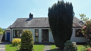 A single-story house with a sloped roof, a chimney, and a front door. There is a well-maintained lawn with a pathway leading to the entrance. - Beck Yeat Cottage - Coniston - close to lake (Coniston)