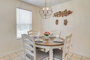 A dining area with a round table, white chairs, a chandelier, and wall art. - Myrtle Beach Condo: Balconies, Walk to Beach! (Myrtle Beach)