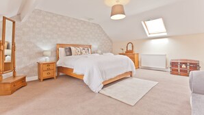 Ein Schlafzimmer mit schrägem Dach, einem Oberlicht, einem Bett mit weißer Bettwäsche, einem hölzernen Nachttisch, einem Schminktisch und einem Heizkörper.