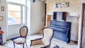 Une pièce avec un piano, deux fauteuils, un lustre et un mur en pierre orné d’œuvres d’art.