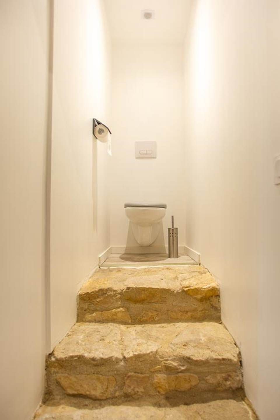 Un escalier étroit menant à des toilettes dans une pièce aux murs blancs.