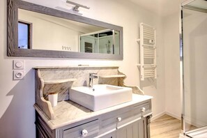 Un baño con tocador de mármol, un espejo grande, un perchero y una zona de ducha.