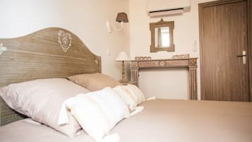 Un dormitorio con cabecera de madera, una cama con ropa blanca, una mesita de noche con lámpara, un espejo y una puerta de madera.