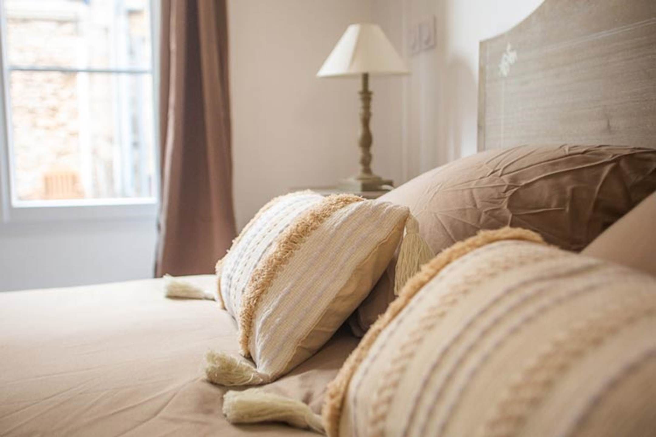 A bed with a headboard, a lamp, and a window with curtains.