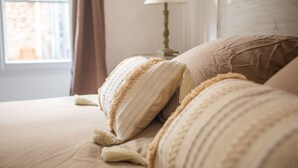 Un lit bien fait, avec une literie et des oreillers de couleur beige, une lampe de chevet et une fenêtre avec des rideaux.