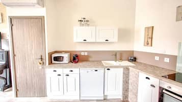 Una cocina compacta con armarios blancos, microondas, cafetera y lavavajillas.