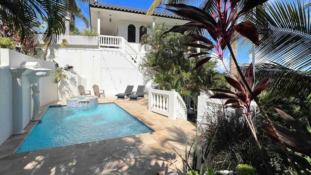 Un espace piscine privé, avec un bâtiment blanc en arrière-plan, entouré d’une végétation tropicale luxuriante.