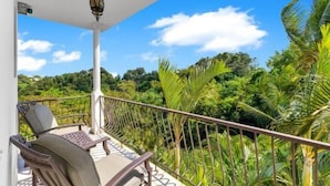 Un balcon avec une chaise et une suspension lumineuse, donnant sur un paysage verdoyant et luxuriant, parsemé de palmiers.
