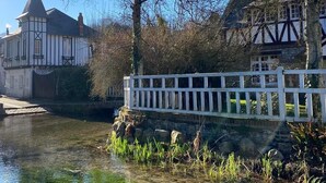 A riverside view with a white bridge, a Tudor-style building, and a modern building with a pointed roof. - "La Chaumière de Nanou", with large garden and close to the sea. (Saint-Valery-en-Caux)