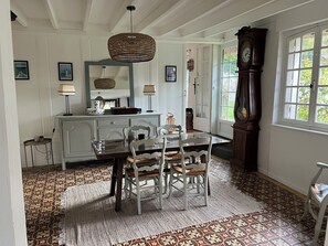 Uma sala de jantar com mesa, cadeiras, luminária pendente, relógio e piso estampado.