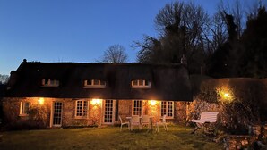 A stone house with a thatched roof, multiple windows, and a small lawn with a table and chairs. - "La Chaumière de Nanou", with large garden and close to the sea. (Saint-Valery-en-Caux)