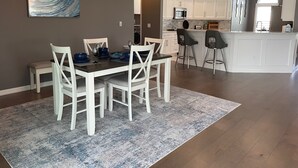 A dining area with a table set for four, white chairs, a blue rug, and a modern chandelier. - Pool, Hot Tub & Golf Views... What More Could You Need?! (The Villages)