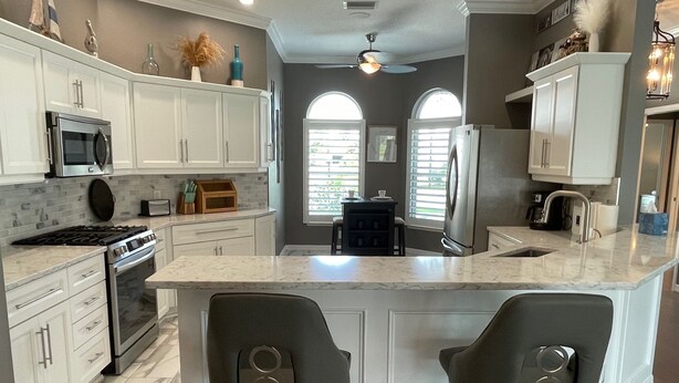 A kitchen with white cabinets, a central island, bar stools, a stove, microwave, and a refrigerator. - Pool, Hot Tub & Golf Views... What More Could You Need?! (The Villages)