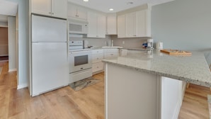 A modern kitchen with white cabinetry, a built-in oven, a microwave, and a coffee maker. - First-Floor Lakefront Gem | Downtown Charlevoix | Pool, Hot Tub, Sauna (Charlevoix)