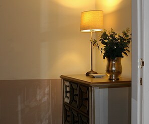 A lamp with a beige shade, a potted plant, and a small white object on a wooden cabinet.