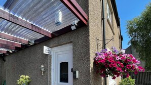 A building with a white door, a sign reading "27a Linden Avenue," and a covered entrance with a metal roof. - Linden Apartment -  an apartment that sleeps 4 guests  in 2 bedrooms (Stirling)