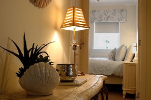 A bedroom with a bed, a bedside table with a lamp, a potted plant, and a window with a view of trees.