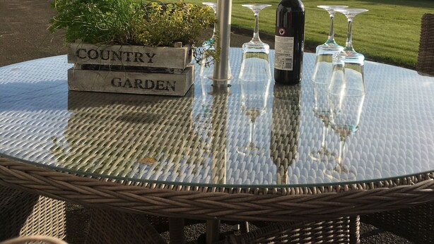 Uma mesa de vidro redonda com um guarda-sol de metal, uma garrafa de vinho e três copos de vinho.