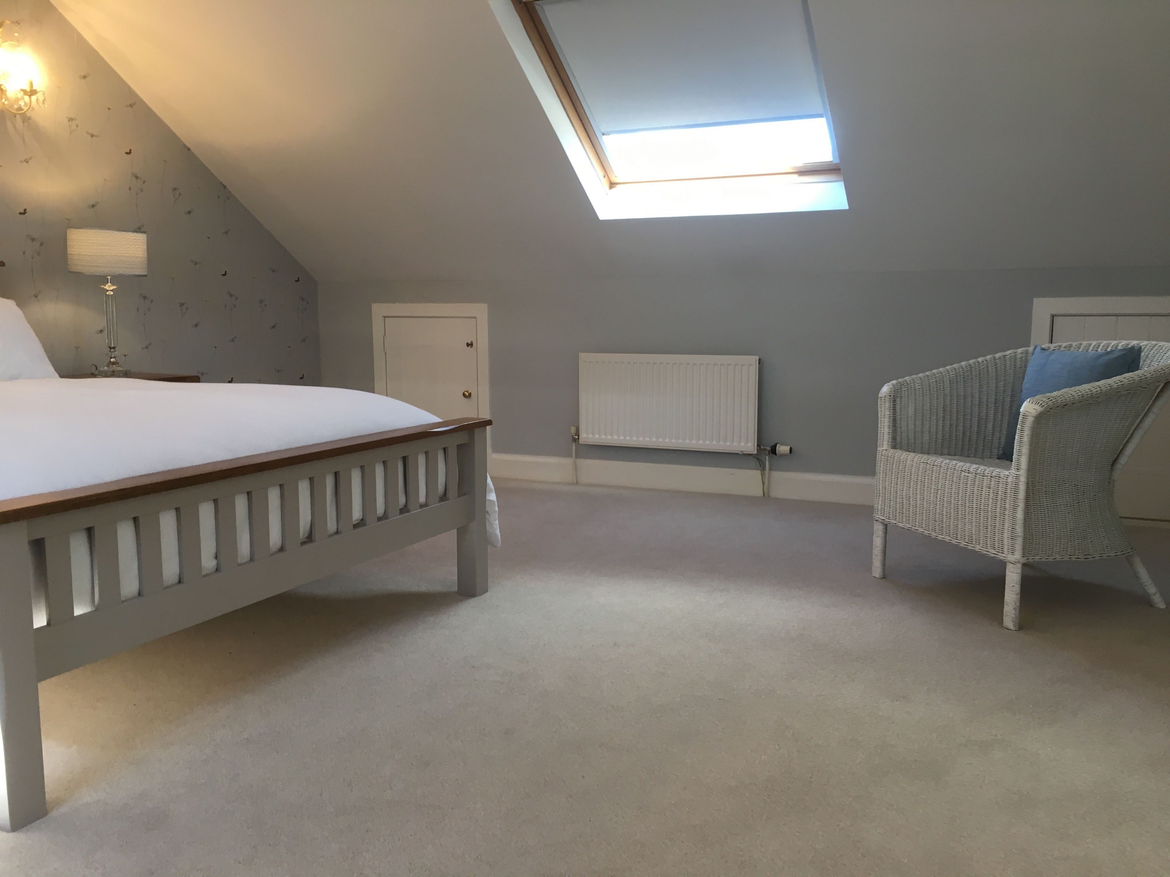 Une chambre avec un plafond en pente, un lit, une chaise, un radiateur et une porte.