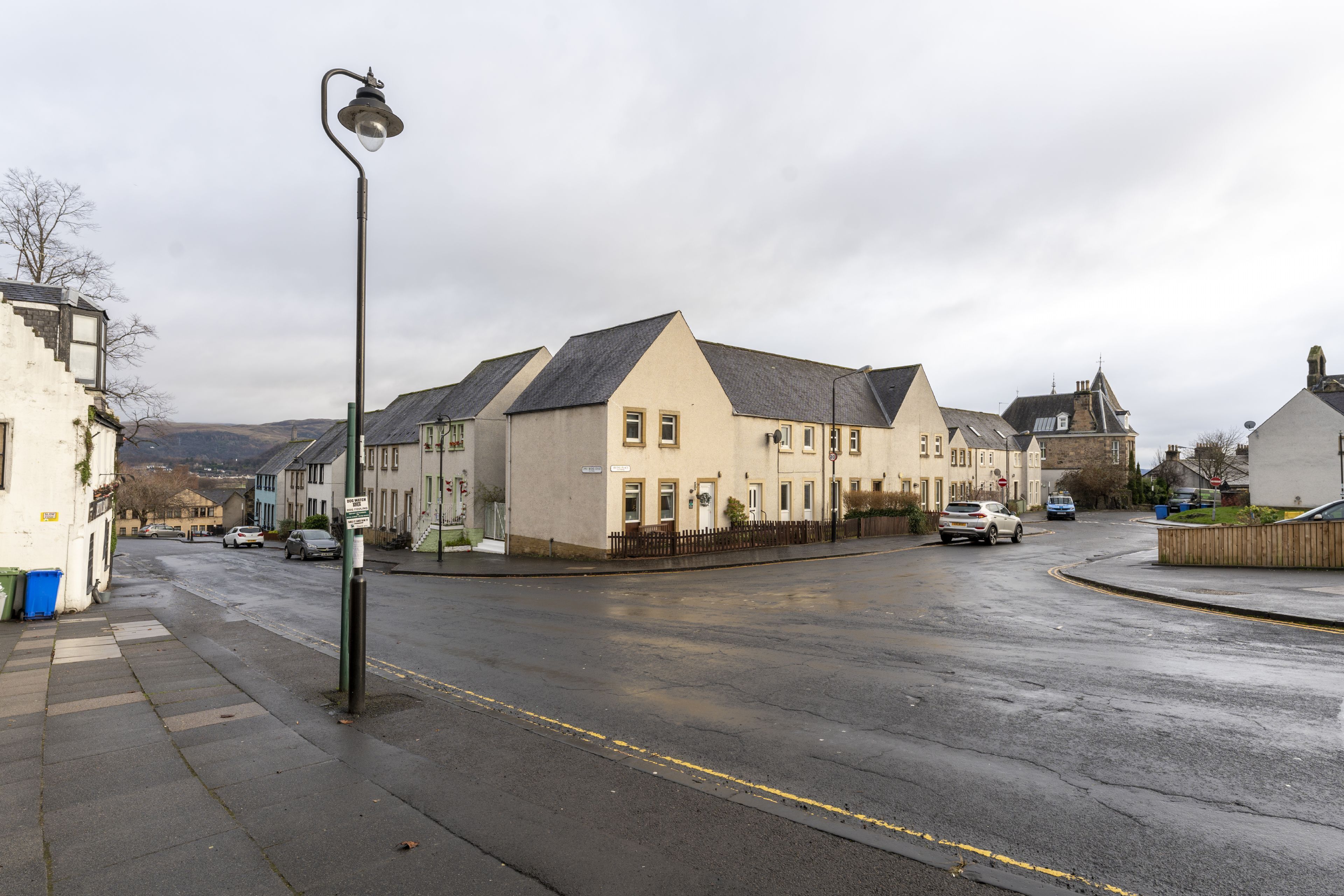 A street with residential buildings, a lamppost, and parked cars.