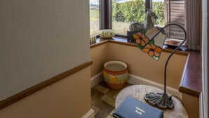 Una habitación con techo de madera, una lámpara de vitral, un libro de visitas sobre una mesita y una ventana con vistas a la vegetación.