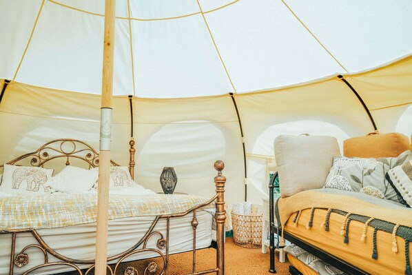 A tent with two beds, each with a wooden frame and white bedding. There is a woven basket and a lamp on one bed.