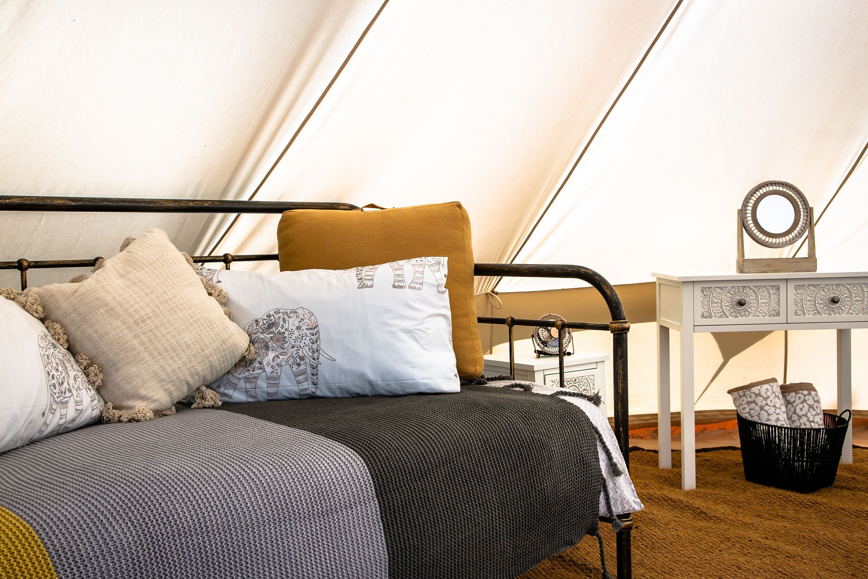A tented room with a bed, pillows, a small table, and a basket.