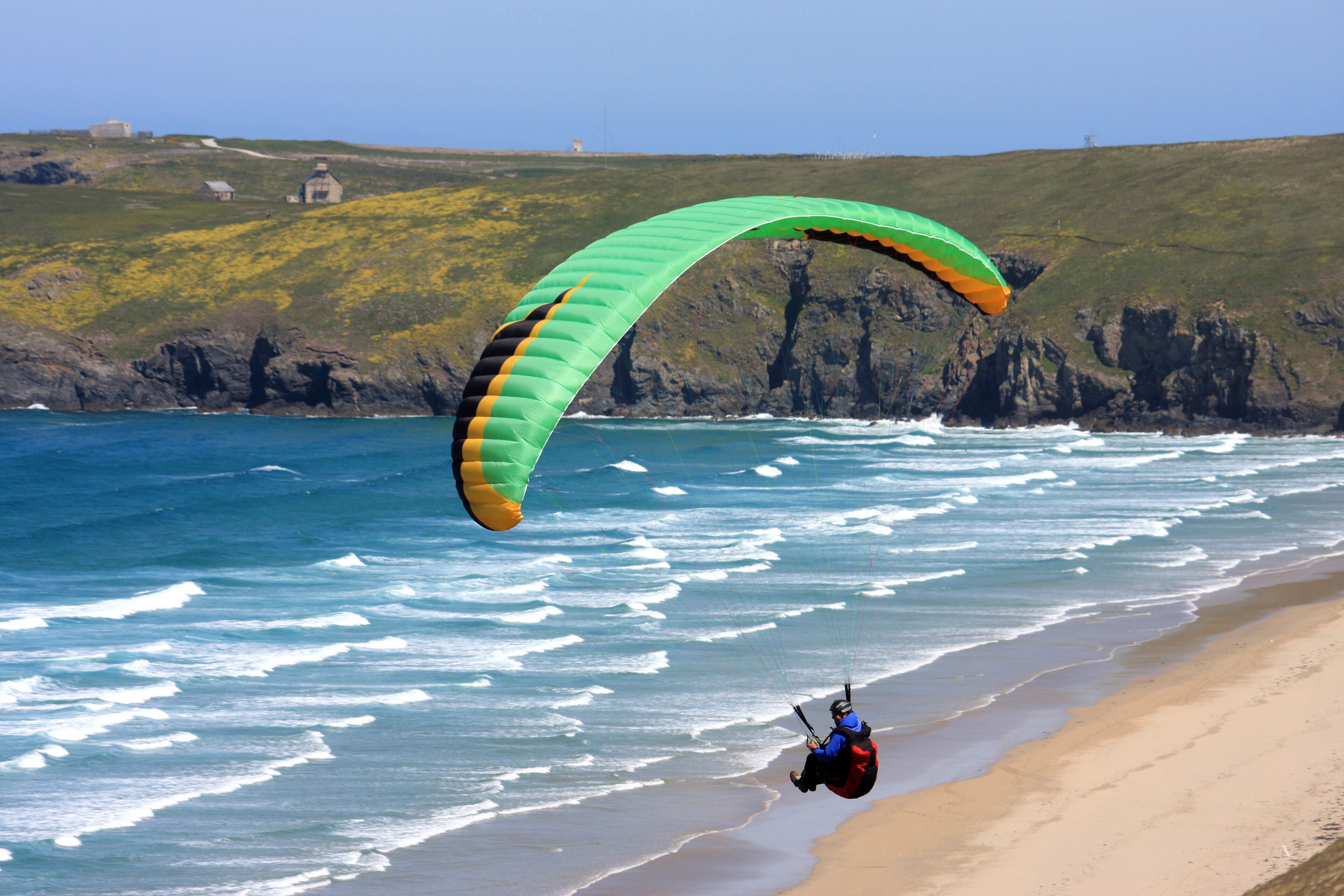 Uma praia com uma pessoa praticando parapente perto da costa.