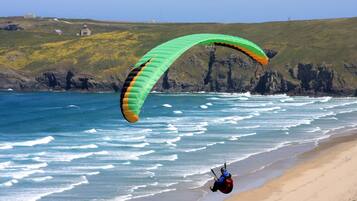 Uma praia com uma pessoa praticando parapente perto da costa.