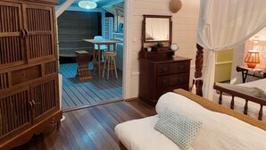 A room with a wooden floor, a bed with a white pillow, a wooden dresser, a small table with chairs, and a mirror on the dresser. - Charming bungalow for 2 with private Jacuzzi (Saint-François)