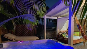 A hot tub with blue lighting, a wooden deck, a hammock, and a covered seating area. - Charming bungalow for 2 with private Jacuzzi (Saint-François)