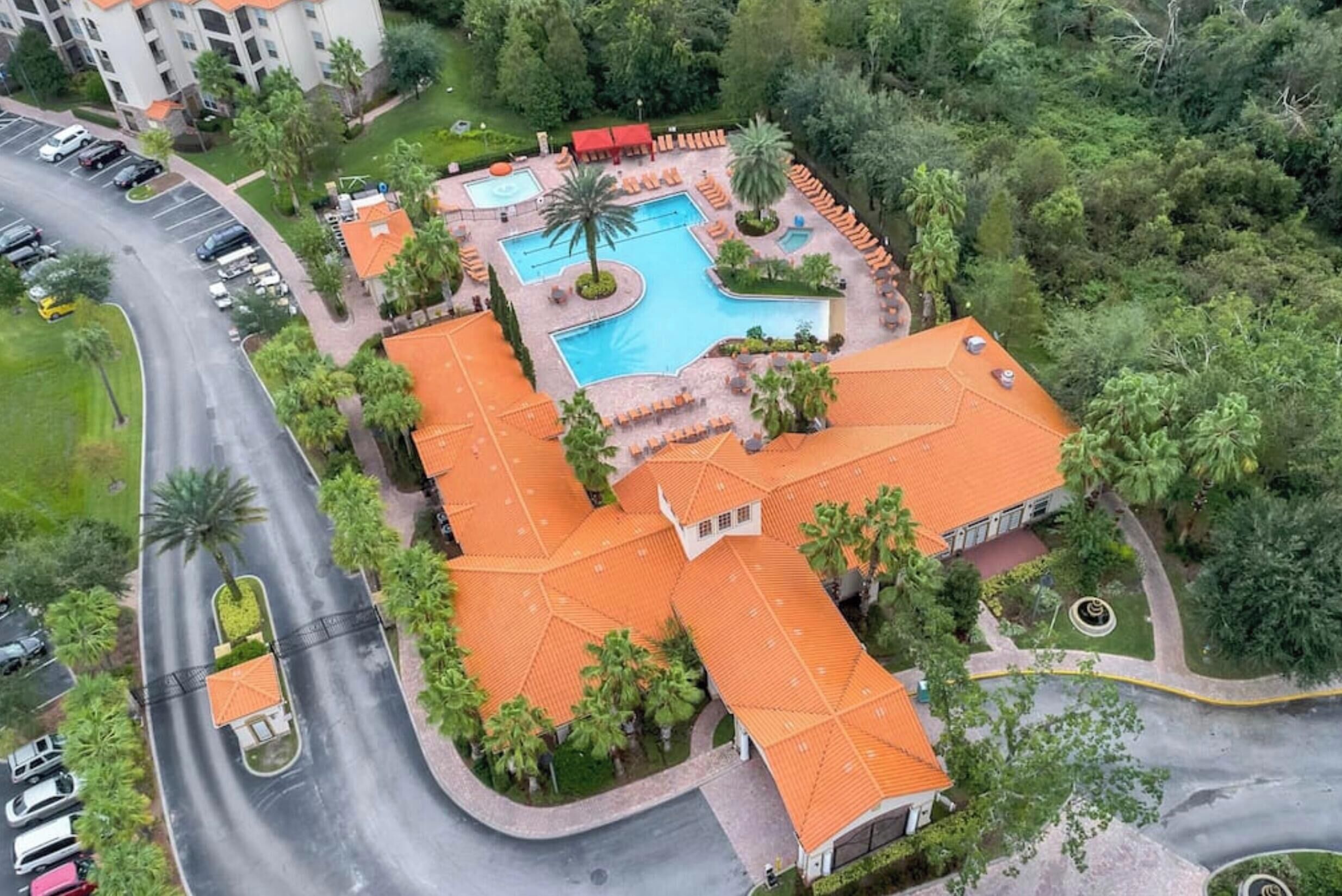An aerial view of a hotel with a swimming pool, palm trees, and a parking lot.