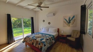 Et soveværelse med seng, stol, natbord, ventilator i loftet og et vindue med gardiner.