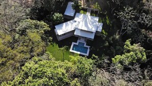 Oversigtsbillede af et moderne hus med swimmingpool omgivet af frodig vegetation.