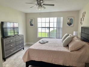 Relax in this serene bedroom with a large bed, flat-screen TV, and stunning views of the surrounding lawn.
