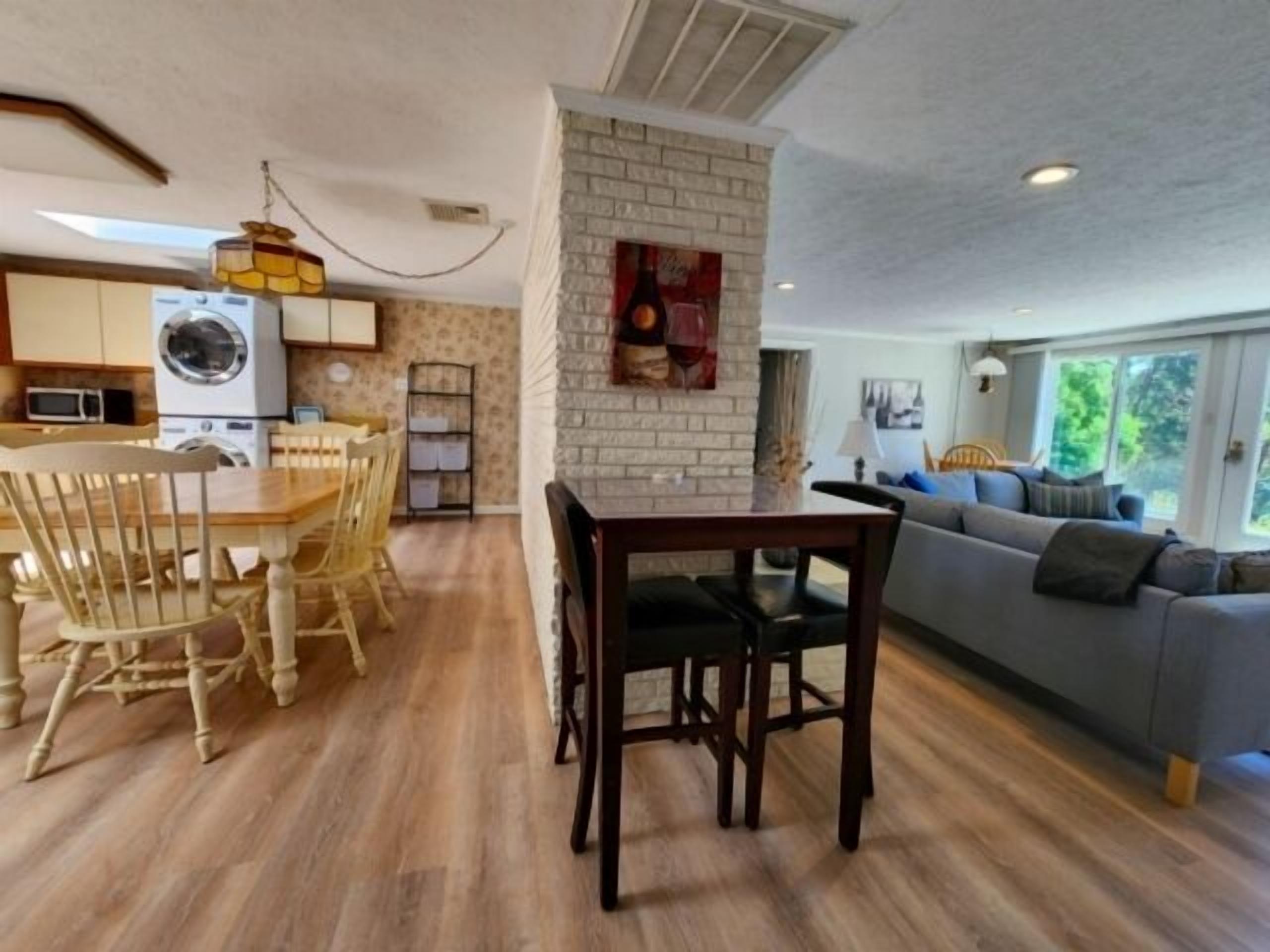 Un comedor con mesa y sillas de madera, una cocina con lavadora y una sala de estar con sofá y ventana.