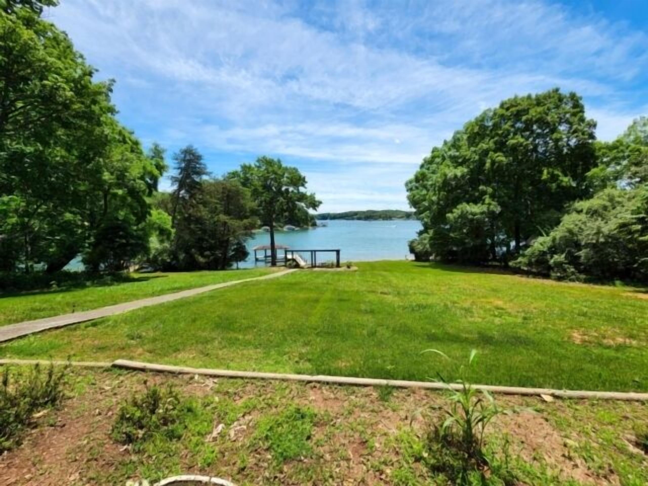 A grassy area with a path leading to a dock by a lake, surrounded by trees.