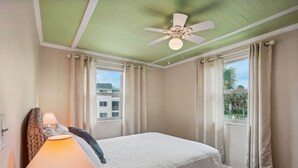 A bedroom with a bed, a ceiling fan, a window with curtains, and a view of buildings outside. - Friendly Native Unit 507- Fun and relaxation on vibrant St Pete Beach! (St Pete Beach)