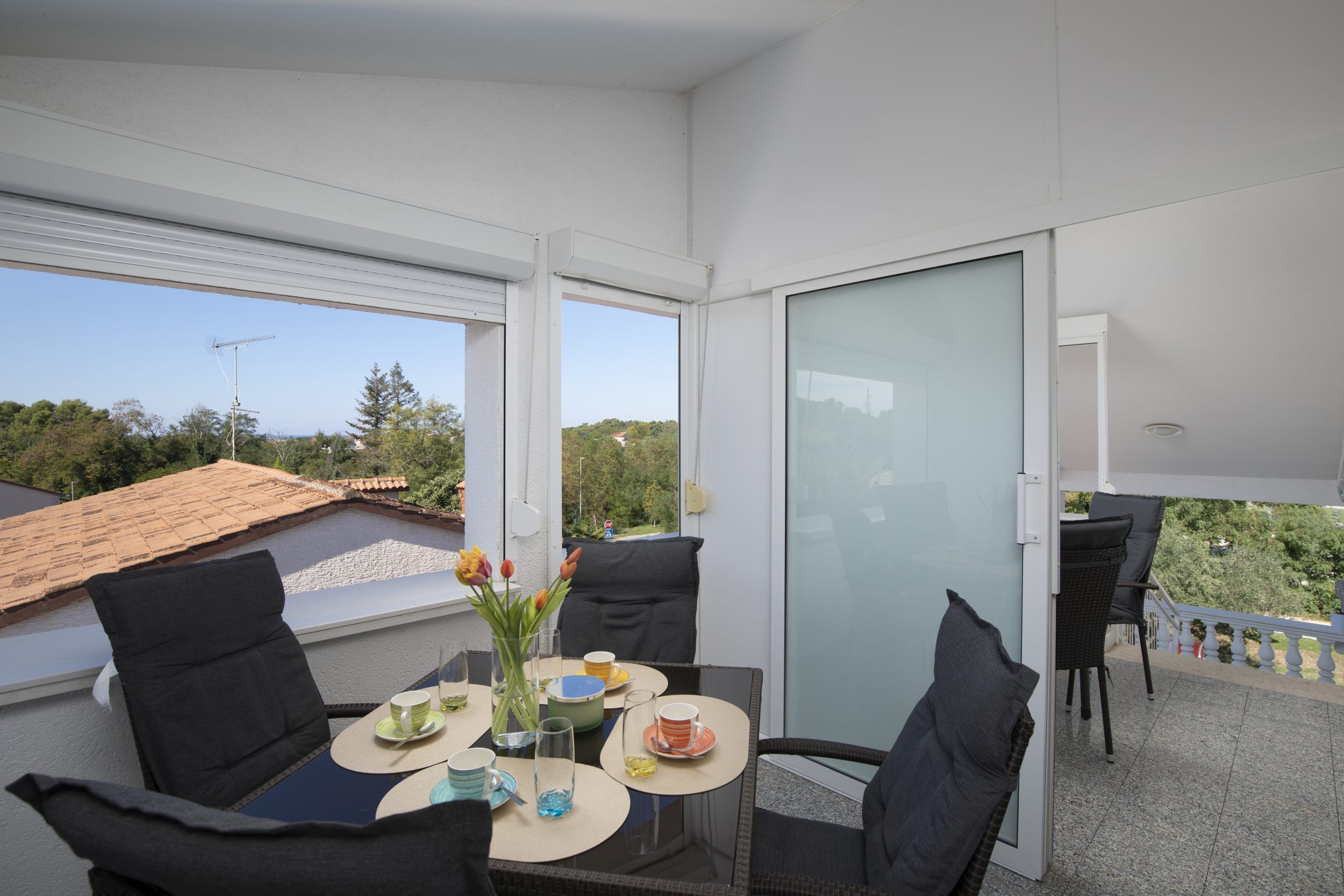 A balcony with a table set for two, chairs, and a view of the surrounding area.