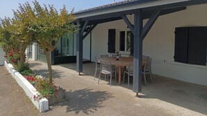 Un espace extérieur aménagé, abrité et doté d’une table et de chaises, entouré d’un jardin planté de fleurs.