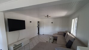 Un salon doté d’un grand téléviseur à écran plat fixé au mur, d’un canapé beige et d’un ventilateur de plafond.