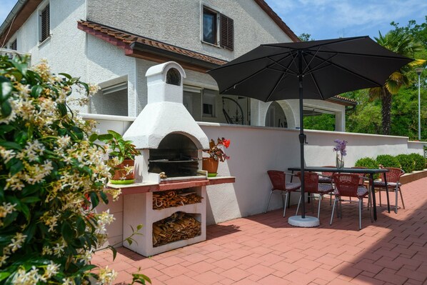 An outdoor patio with a brick floor, a white oven, and a table with chairs.