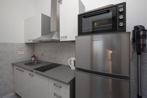 A kitchen with a stainless steel refrigerator, a built-in microwave, a kettle, and a sink.